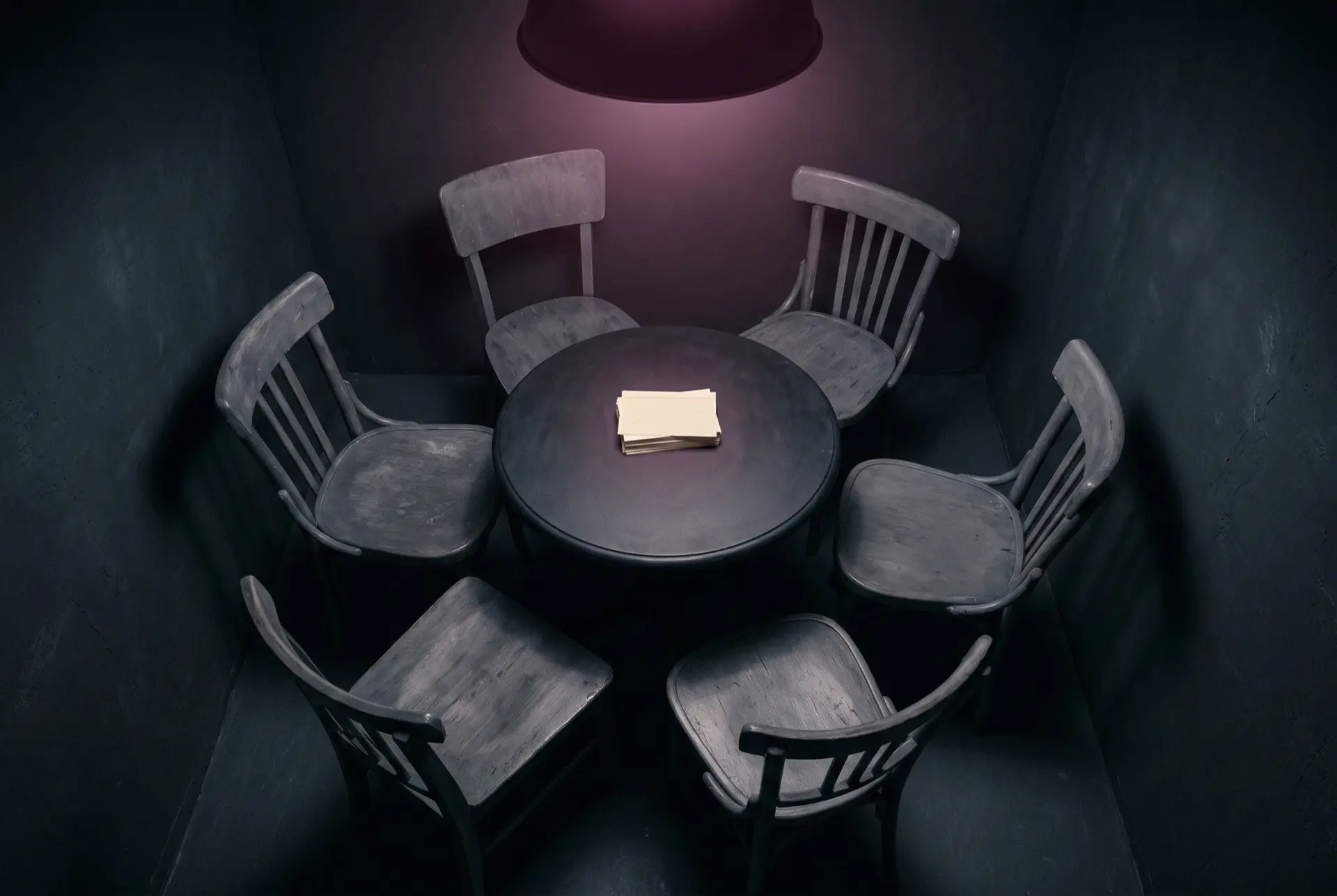 Six empty chairs around a small round table with a stack of blank cards under a lamp